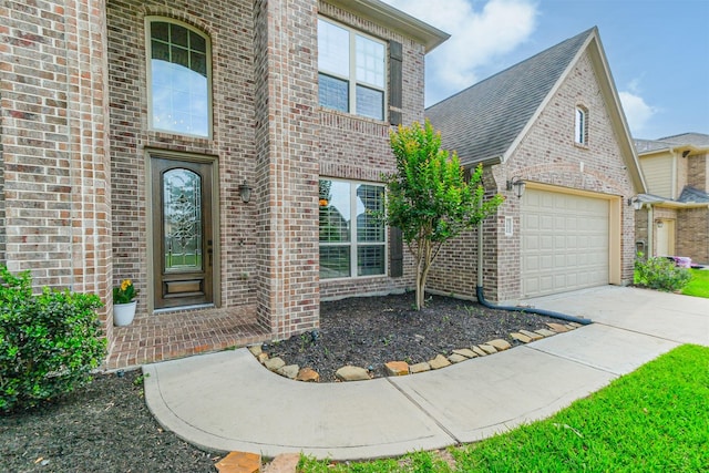 doorway to property with brick siding, an attached garage, and driveway