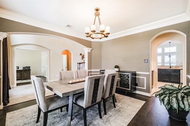 dining area featuring wainscoting, a chandelier, arched walkways, ornamental molding, and decorative columns