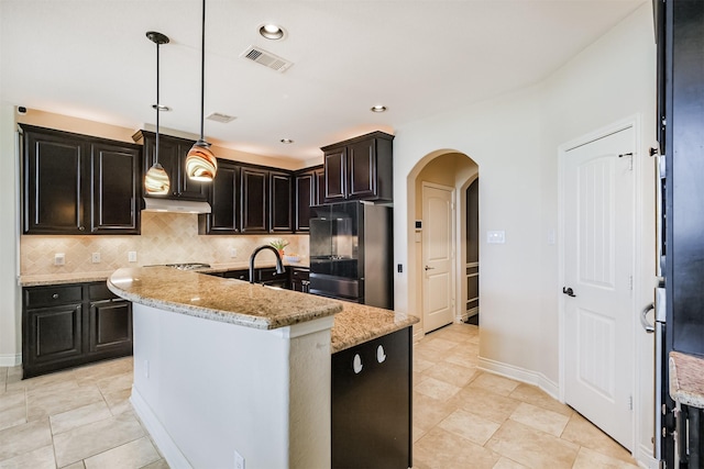 kitchen featuring under cabinet range hood, smart refrigerator, visible vents, arched walkways, and a kitchen island with sink