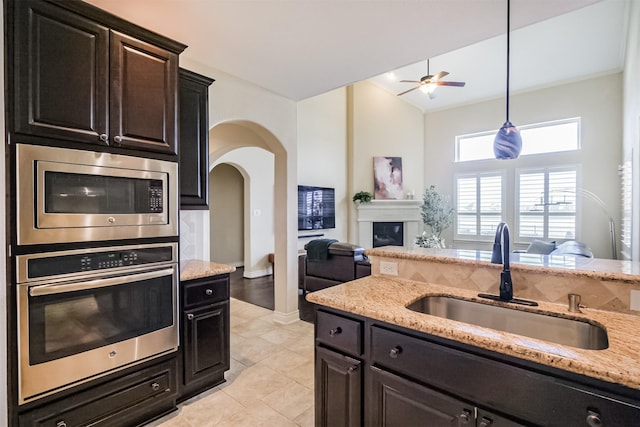 kitchen featuring light stone counters, stainless steel appliances, a ceiling fan, a sink, and open floor plan