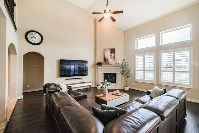 living area with ornamental molding, arched walkways, baseboards, high vaulted ceiling, and ceiling fan