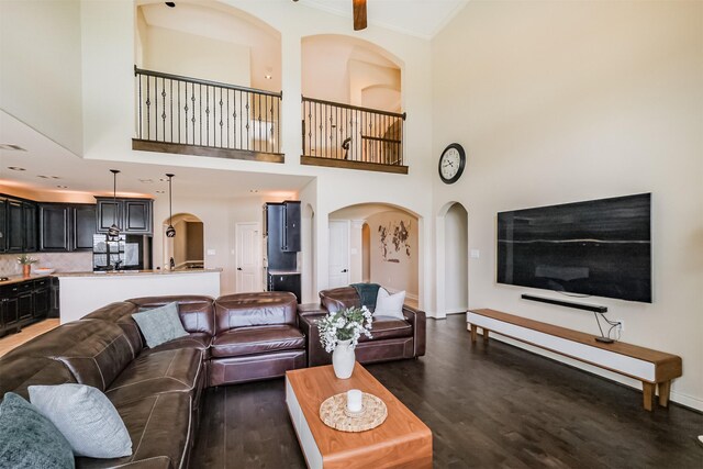 living room with a towering ceiling, wood finished floors, arched walkways, and ornamental molding