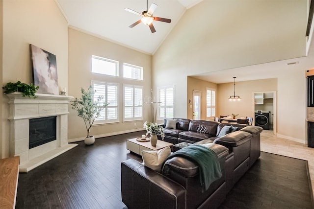 living area with high vaulted ceiling, ceiling fan with notable chandelier, a glass covered fireplace, washer / dryer, and baseboards