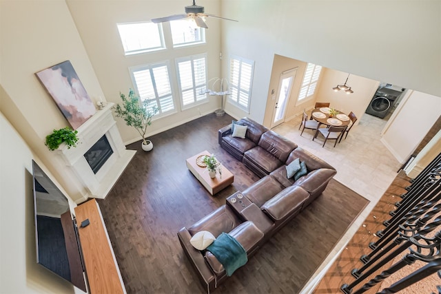 living room with wood finished floors, a glass covered fireplace, ceiling fan, a towering ceiling, and baseboards