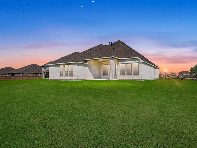 rear view of house with brick siding, a lawn, and fence
