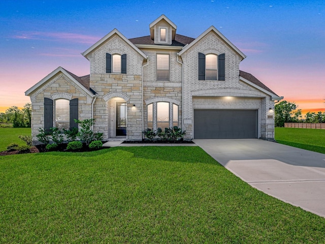 french country style house featuring roof with shingles, driveway, stone siding, a garage, and a yard