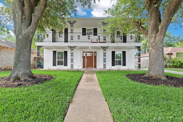 view of front facade featuring a front yard, a balcony, and brick siding