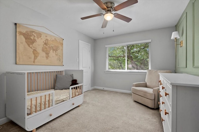 bedroom with light colored carpet, a nursery area, baseboards, and a ceiling fan