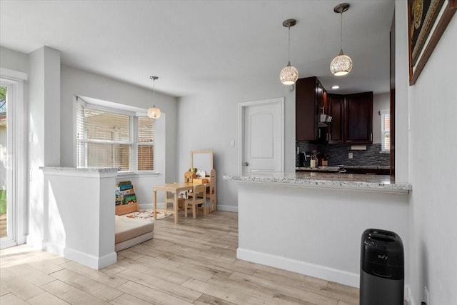 kitchen featuring dark brown cabinets, baseboards, light wood-style floors, backsplash, and light stone countertops