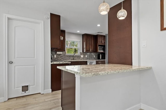 kitchen featuring stainless steel appliances, a sink, light wood-style flooring, a peninsula, and tasteful backsplash