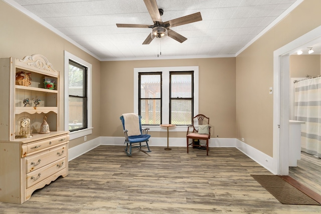 living area featuring baseboards, ornamental molding, a ceiling fan, and wood finished floors