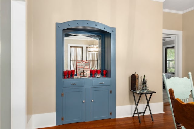 bar featuring crown molding, dark wood-style flooring, baseboards, and indoor bar