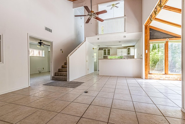 unfurnished living room with ceiling fan, a towering ceiling, stairs, and plenty of natural light
