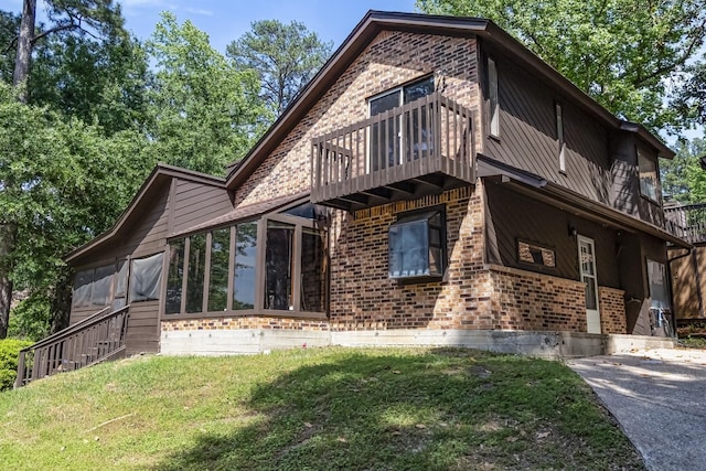 exterior space featuring a front lawn, a sunroom, brick siding, and a balcony