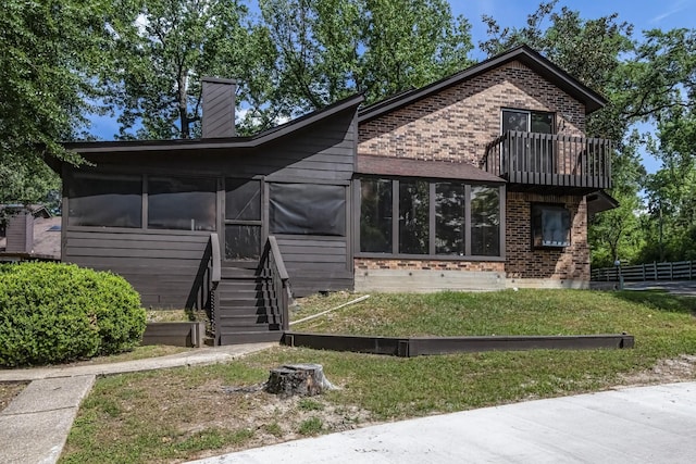 view of front of house with stairway, a chimney, a sunroom, and brick siding