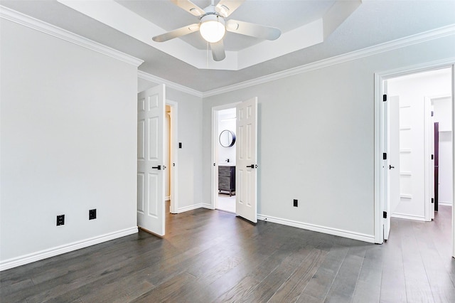 empty room with ceiling fan, dark wood finished floors, baseboards, a tray ceiling, and crown molding