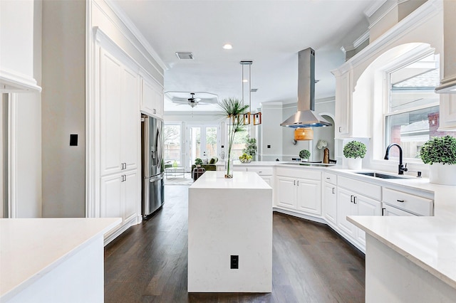 kitchen featuring stainless steel fridge, island range hood, a sink, a ceiling fan, and light countertops
