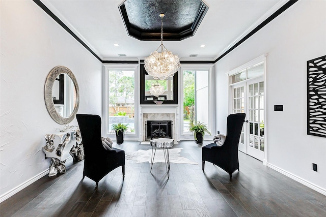 living area with a chandelier, wood finished floors, crown molding, a tray ceiling, and baseboards