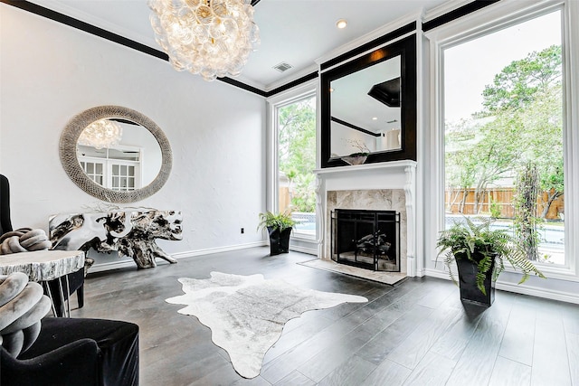 living area featuring a chandelier, crown molding, plenty of natural light, a high end fireplace, and wood finished floors