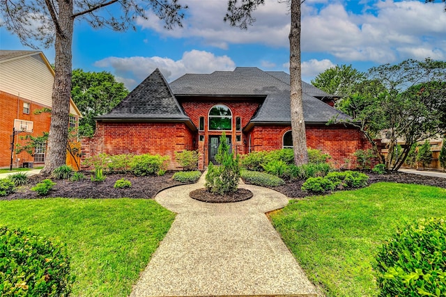 view of front of house featuring roof with shingles, brick siding, and a front lawn