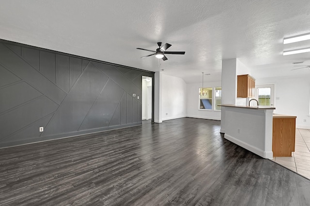 unfurnished living room featuring a textured ceiling, a ceiling fan, baseboards, and dark wood-style flooring