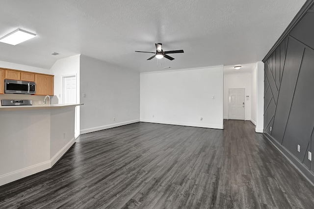 unfurnished living room featuring a textured ceiling, a sink, dark wood-style flooring, baseboards, and a ceiling fan