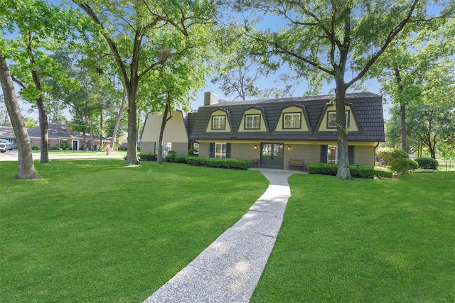 view of front facade featuring a front lawn, brick siding, mansard roof, and a chimney