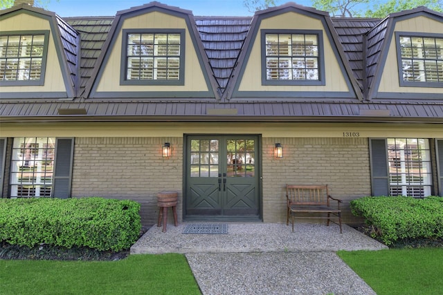 view of exterior entry featuring brick siding, a gambrel roof, and metal roof