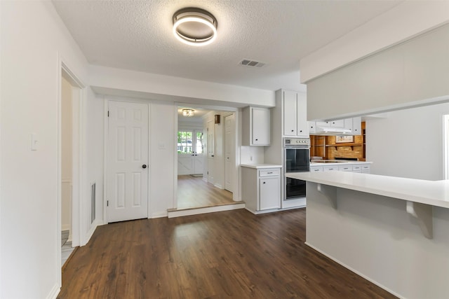 kitchen with light countertops, double oven, a textured ceiling, and dark wood-style floors