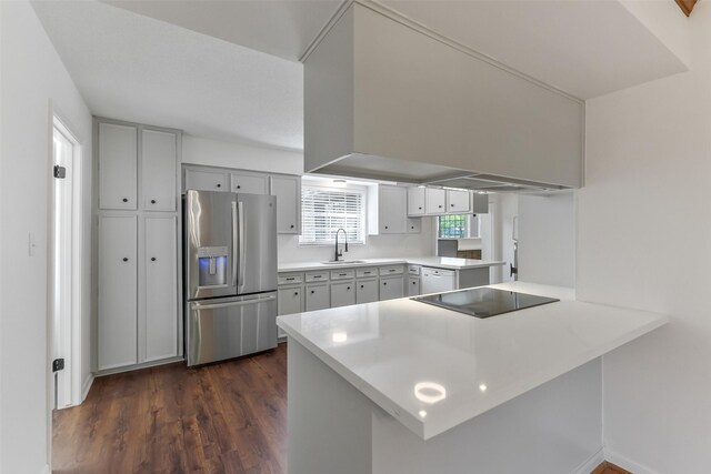 kitchen featuring a sink, stainless steel fridge, light countertops, dark wood finished floors, and a peninsula