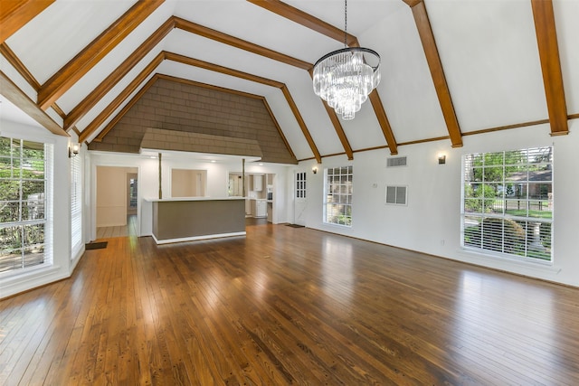 unfurnished living room featuring high vaulted ceiling, plenty of natural light, hardwood / wood-style flooring, an inviting chandelier, and visible vents