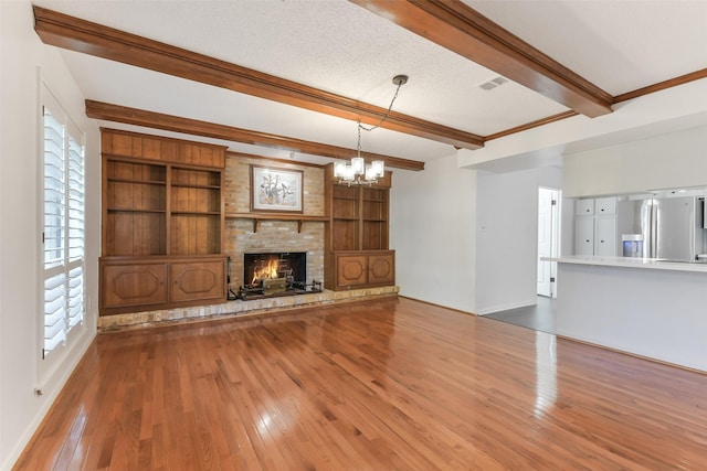 unfurnished living room with wood finished floors, baseboards, a notable chandelier, beam ceiling, and visible vents