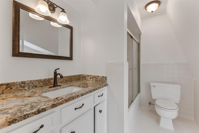 bathroom featuring tile patterned flooring, a wainscoted wall, toilet, vanity, and tile walls