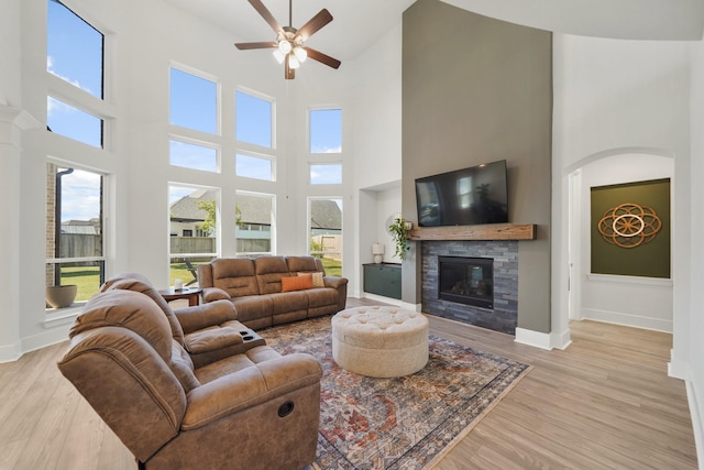 living room featuring a high ceiling, a ceiling fan, a glass covered fireplace, and light wood-style floors