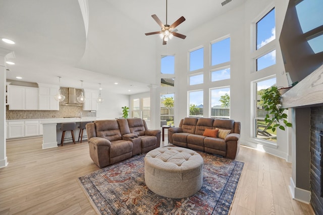 living area with a high ceiling, a ceiling fan, light wood finished floors, and decorative columns