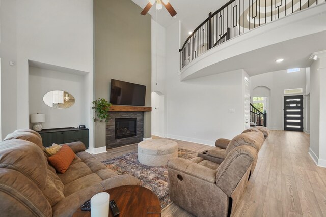 living area with a glass covered fireplace, wood finished floors, a towering ceiling, and a ceiling fan
