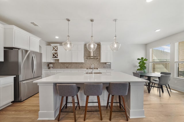 kitchen featuring backsplash, visible vents, a sink, freestanding refrigerator, and a center island with sink