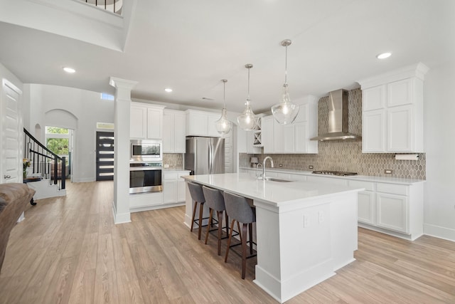kitchen with wall chimney exhaust hood, light wood-style flooring, a sink, and appliances with stainless steel finishes