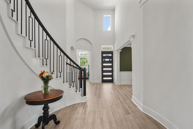 entrance foyer with wood finished floors, stairs, a towering ceiling, and baseboards