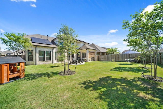 rear view of house featuring a fenced backyard, brick siding, a yard, roof mounted solar panels, and a patio