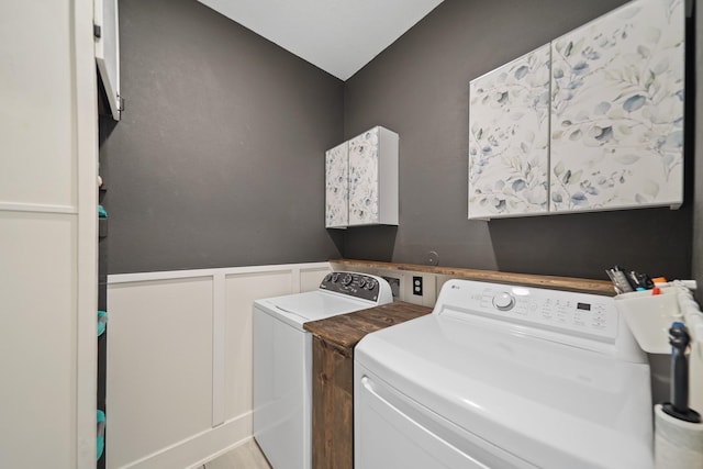 clothes washing area with separate washer and dryer, wainscoting, and a decorative wall