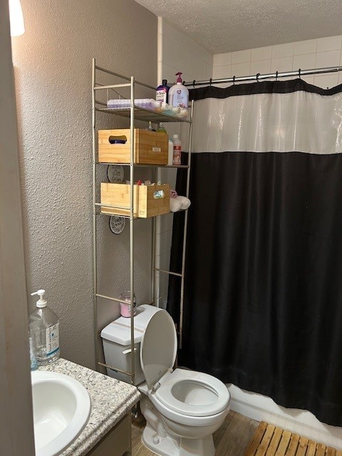 bathroom with a textured wall, a textured ceiling, toilet, a shower with curtain, and vanity
