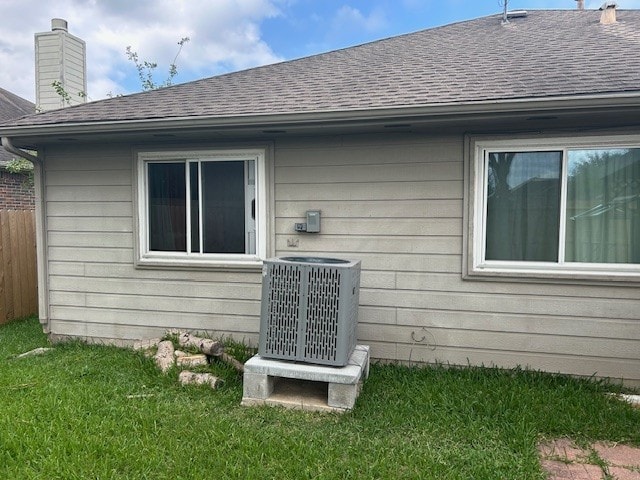 view of side of property with roof with shingles, central AC, and a chimney