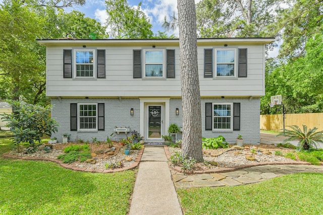 colonial home featuring brick siding, fence, and a front yard