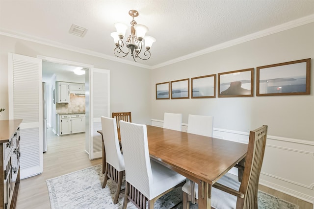 dining space with a textured ceiling, light wood-type flooring, visible vents, a chandelier, and crown molding