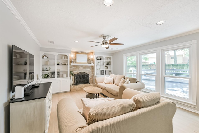 living room featuring a ceiling fan, crown molding, a textured ceiling, light wood-type flooring, and a fireplace