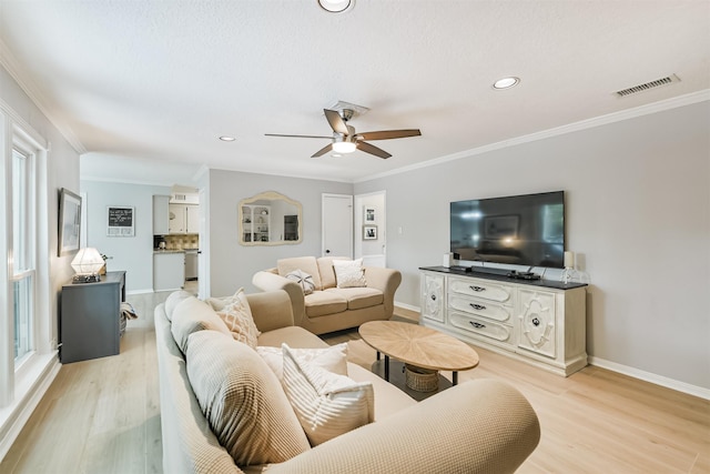 living room with light wood-type flooring, baseboards, visible vents, a ceiling fan, and crown molding
