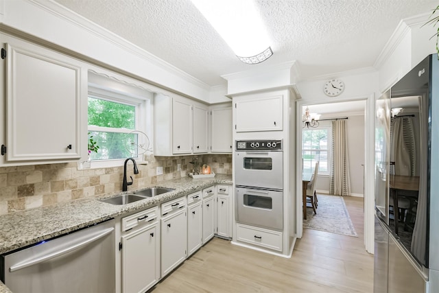 kitchen with stainless steel appliances, a sink, a textured ceiling, light wood-type flooring, and light stone counters