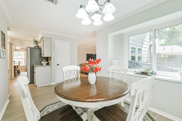 dining room with a chandelier, light wood finished floors, baseboards, ornamental molding, and visible vents