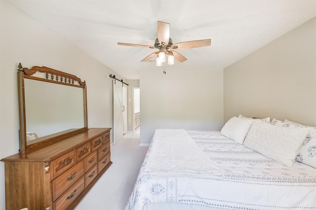 carpeted bedroom featuring a barn door and a ceiling fan